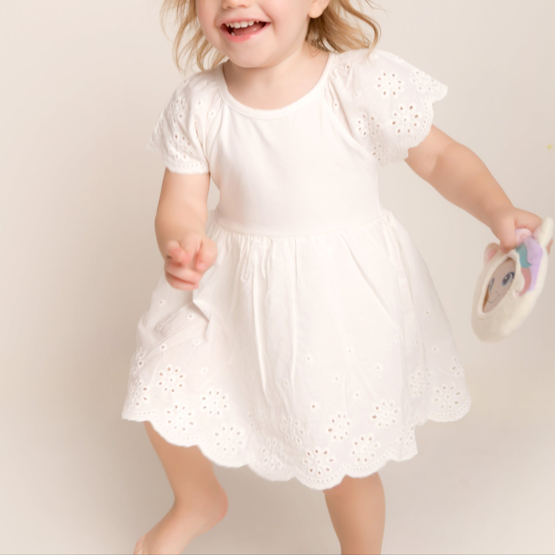 Child in a white dress standing against a plain background